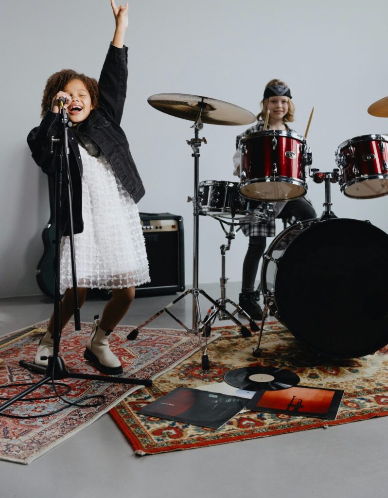 pexels photo 9644675 9644675 Two young girls perform energetically in a music band with drums and a microphone.